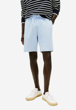Shorts en coton bleu clair avec une taille élastique et un cordon de serrage, présentants une coupe décontractée et des poches latérales, associés à des baskets blanches.
