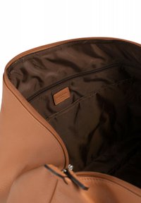 Borsa in pelle color tan con una texture liscia, dotata di un interno in tessuto marrone, chiusura con zip e una piccola etichetta con logo nella tasca interna.