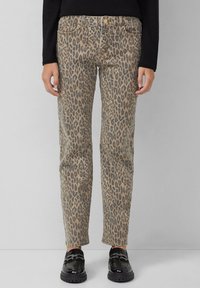 Pantaloni a stampa leopardata in beige e marrone, realizzati in denim, con taglio dritto, design a cinque tasche e cuciture a contrasto. Calzature nere visibili.