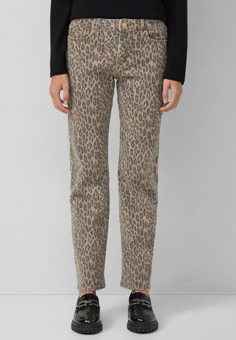Pantaloni a stampa leopardata in beige e marrone, realizzati in denim, con taglio dritto, design a cinque tasche e cuciture a contrasto. Calzature nere visibili.