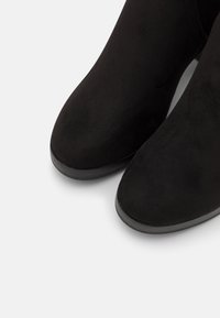 Černé kotníkové boty z semiše s kulatou špičkou, hladkou texturou a nízkým gumovým podpatkem, s minimalistickým designem a bez viditelného kovového doplňku.