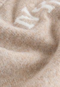 Pehme beežikas kudumkangas koos peenete osaliselt nähtavate valgete tähtedega, mis näitab tekstuurse lõnga ja õrnaid voltse.