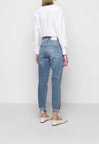 Jeans en denim bleu clair avec une coupe droite, ourlet brut et deux poches arrière. Associé à une chemise blanche à boutons et des ballerines beiges.