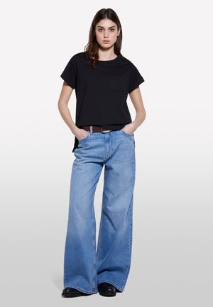 T-shirt noir à manches courtes avec une poche sur la poitrine, associé à un jean large bleu clair et des bottes noires. Design simple et décontracté.