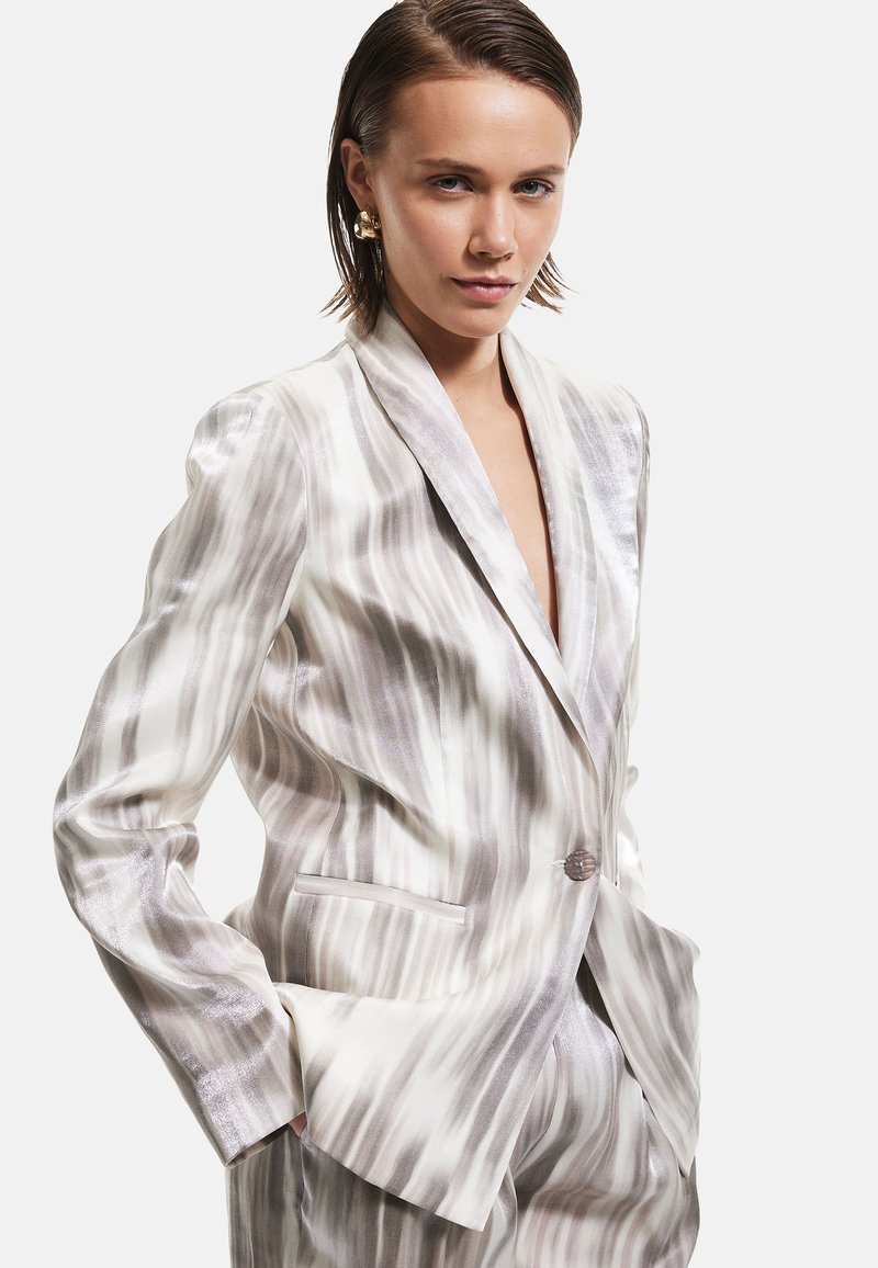 Blazer en tissu léger et soyeux avec un motif de rayures ondulées blanches et grises. Il possède un col à revers, une fermeture à bouton unique et des poches.