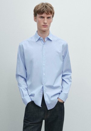 Camicia azzurro chiaro a righe con colletto, maniche lunghe e vestibilità comoda, abbinata a pantaloni scuri. Tessuto dalla superficie liscia.