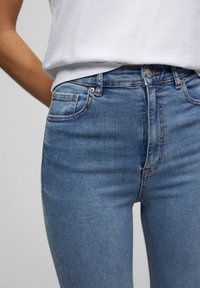 Jeans de mezclilla azul claro con un corte ajustado, que presentan bolsillos estándar, un desvanecimiento sutil y costuras clásicas a lo largo de las costuras.