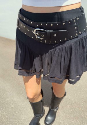 Black pleated skirt with a textured hem, paired with a wide black leather belt featuring metallic studs and a silver buckle, and black boots.