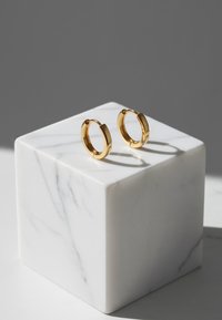 Gyllene hoopsörhängen med en polerad yta, visade på en vit marmorblock, med en slät, cirkulär form och sömlös design.