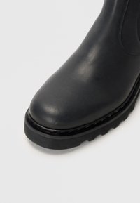 Botte de cheville en cuir noir avec un bout rond, un dessus texturé et une semelle en caoutchouc épaisse dotée de petites rainures pour l'adhérence.