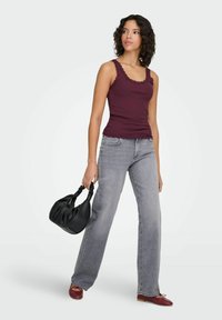 Bordeauxrood geribd tanktop met kanten rand, grijze jeans met wijde pijpen, rode ballerina's en een zwarte plissé handtas.