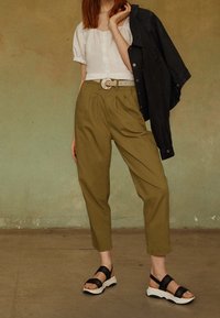 Chaqueta de mezclilla negra, blusa blanca de botones de manga corta, pantalones de tiro alto verde oliva y sandalias negras con suelas blancas.