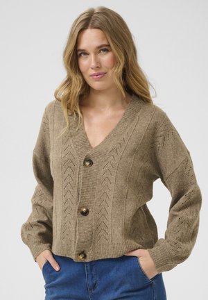 Beige strikket cardigan med v-hals, lange ærmer og pilmønstre. Har fire flade knapper og et cropped design. Blød tekstur.