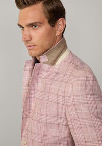 Veste à carreaux rose clair avec une finition texturée, col marron contrastant et détails de boutons subtils. Coupe ajustée avec un design moderne.