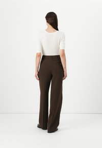 Pantaloni larghi marroni con una vestibilità sartoriale, caratterizzati da una texture liscia e due tasche posteriori. Abbinati a un top bianco aderente.