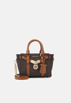 Lille Michael Kors håndtaske i mørkebrun monogrammønster med beige læderhåndtag, rem og guldfarvet låsevedhæng foran.