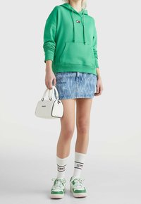 Sudadera verde con capucha, falda de mezclilla, bolsa blanca con acentos negros, calcetines blancos con logo, zapatillas verde y blancas. Materiales texturizados.