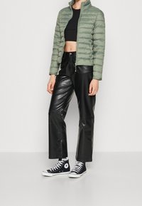 Wypełniona zielona kurtka z wysokim kołnierzem, połączona z czarnymi skórzanymi spodniami o wysokim stanie i czarnymi trampkami Converse z białymi akcentami.