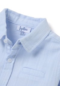 Lichtblauw kortemouwenshirt van gestructureerde stof, voorzien van een kraag, twee knopen en een klein borstzakje met subtiele stiksels.
