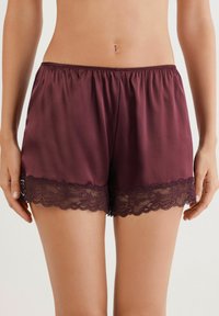 Bordeaux satijnen shorts met een elastische tailleband en delicate zwarte kanten trim aan de onderranden. Soepele textuur en comfortabele pasvorm.