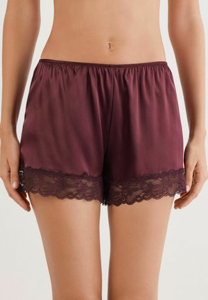 Burgundyröda satängshorts med elastisk midja och delikat svart spetsdetalj i nederkanten. Slät textur och avslappnad passform.