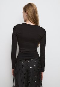 Črni dolg rokav srajca iz elastičnega materiala, prilegajoč dizajn. Nošena z teksturirano črno krilo, ki ima bleščeče cvetlične vzorce.