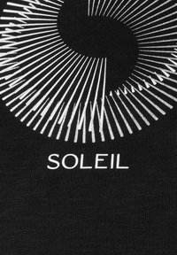 Tissu noir avec un graphique circulaire blanc composé de lignes rayonnantes, présentant le mot "SOLEIL" imprimé en dessous dans une police en gras.