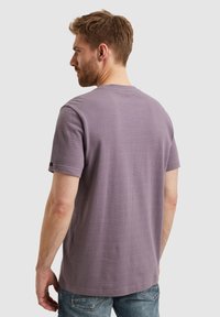Camiseta de manga corta color púrpura con un patrón texturizado, escote redondo y corte relajado, combinada con jeans azules.