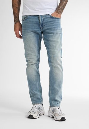 Light blue denim jeans with a slim fit, faded texture, and front pockets. Worn with white athletic shoes.