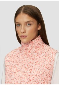Roze en witte gebreide turtleneck trui met een gestructureerd patroon en een hoge kraag. Gemaakt over een witte langemouwen top.