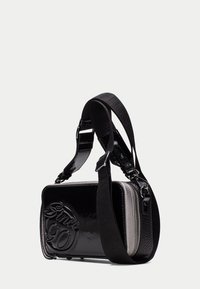 Borsa a tracolla in pelle verniciata nera con finitura lucida, caratterizzata da un lato testurizzato e dettaglio in rilievo "Since 90" sul frontale. Tracolla regolabile.