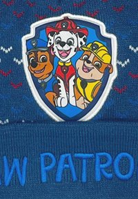 Niebieska dziana czapka beanie z wypukłą łatą, na której znajdują się trzy kreskówkowe psy. Na dole wyszyty jest napis "PAW PATROL" w jaskrawym niebieskim kolorze.