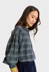 Camicia a maniche lunghe a quadri blu navy con linee verdi, blu e gialle, dotata di scollo henley con bottoni e maniche a sbuffo.