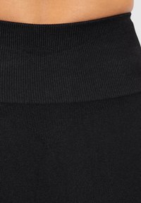 Czarne legginsy z teksturowanym, prążkowanym pasem i gładkim korpusem. Materiał wydaje się elastyczny, zaprojektowany z myślą o komforcie i swobodzie ruchów.