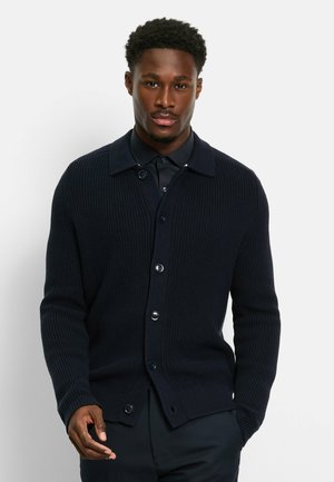 Navy blue ribbed knit cardigan with a collared neckline, front button closure, and textured sleeves, worn over a navy shirt.