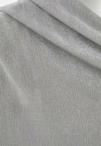 Zložená svetlo šedá tkanina s jemnou vertikálnou pruhovanou textúrou a subtílnym heather vzorom, zdôrazňujúca jemnosť a pružnosť.