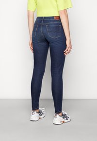 Mörkblå denim skinny jeans med bakfickor, lätt sömnadsdetalj och en brun läderlapp vid midjan.