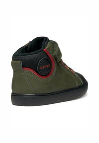 Zapatilla alta de ante verde con detalles de malla negra y costuras rojas. Presenta una correa de Velcro y un diseño de suela redondeada para mayor soporte.