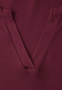 Primer plano de tela burdeos con un detalle de costura en forma de V, mostrando la textura y las puntadas en un material de punto suave.