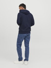 Haut à capuche bleu marine avec un cordon de serrage, associé à un jean en denim bleu et des baskets blanches. Modèle de dos, mettant en valeur les détails du vêtement.
