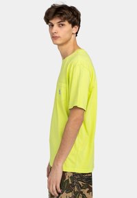 Neon yellow short-sleeve t-shirt with a chest pocket and crew neckline; paired with patterned camo shorts. Smooth texture, relaxed fit.