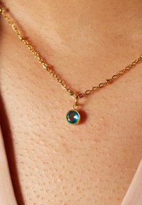 Gouden ketting met een ronde, gefacetteerde turquoise edelsteen hanger. De hanger heeft een diameter van ongeveer 1 cm.