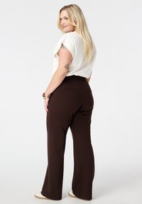 Romige kortekorte mouwtop in combinatie met bruine, high-waisted broek met een relaxte pasvorm en elastische tailleband, tegen een witte achtergrond.