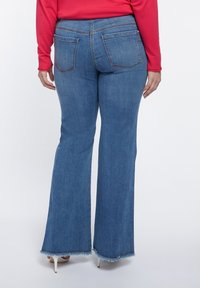 Modré rozšířené džíny s roztrhnutým lemem, vyrobené ze středně těžké denimové látky a se dvěma zadními kapsami. V kombinaci s červeným topem.