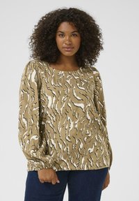 Blusa a maniche lunghe in tessuto beige con un motivo ondulato bianco e nero, colletto rotondo e polsini arricciati con elastico.