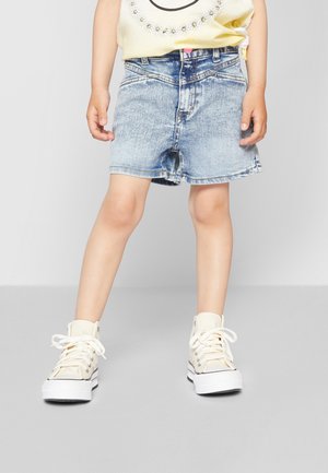 Shorts en denim bleu délavé avec une coupe droite, portés avec des baskets montantes beiges. Dotés d'un bouton rose et d'un léger effilochage à l'ourlet.