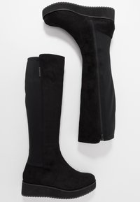Zwart kniehoge laarzen met een suede afwerking, een gestructureerde plateauzool en een ritssluiting aan de zijkant, voorzien van een gladde stofpaneel.