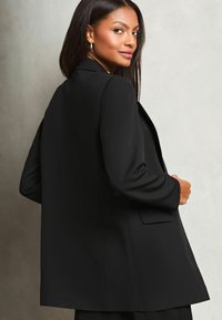 Must西外, mille fit with a smooth texture, ühe nupuga sulgemine ja lõigatud kraed. Omab külje taskuid ja selja venti.