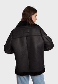 Black leather jacket with a textured finish, featuring a wide shearling collar and a cropped hem. Visible stitching and side pockets.