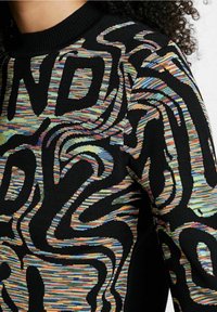 Pull noir présentant un motif abstrait multicolore vibrant en texture tissée, avec un col côtelé et des manches longues.